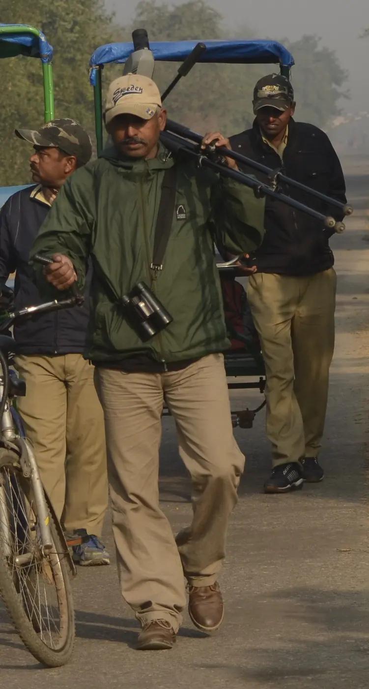 A local bird guide walking with a spotting scope on a tripod over his shoulder and binoculars round his neck