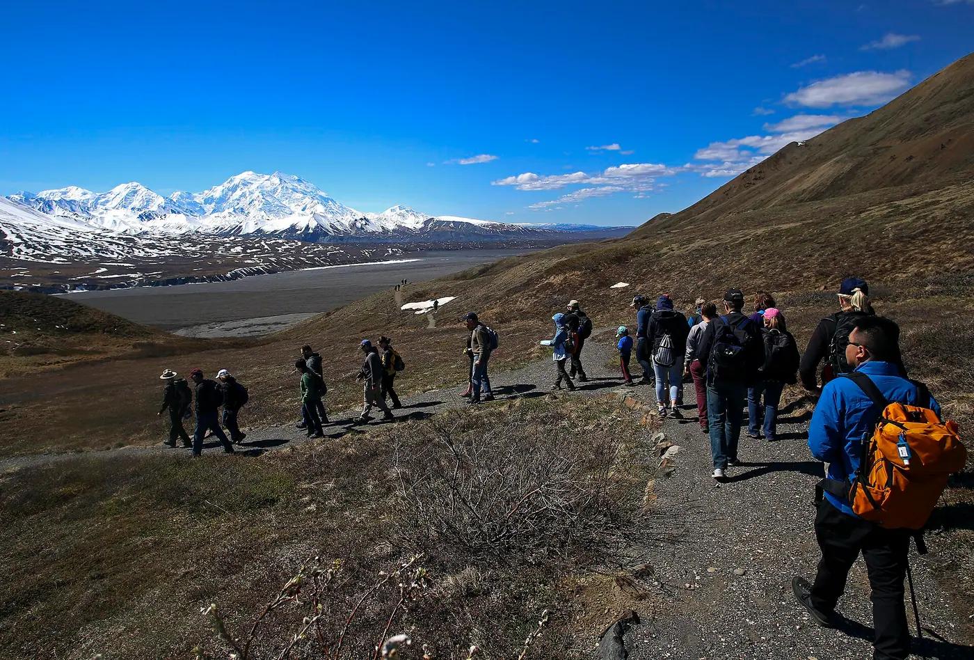 A park ranger leads a line of visitors along a gravel trail across open tundra