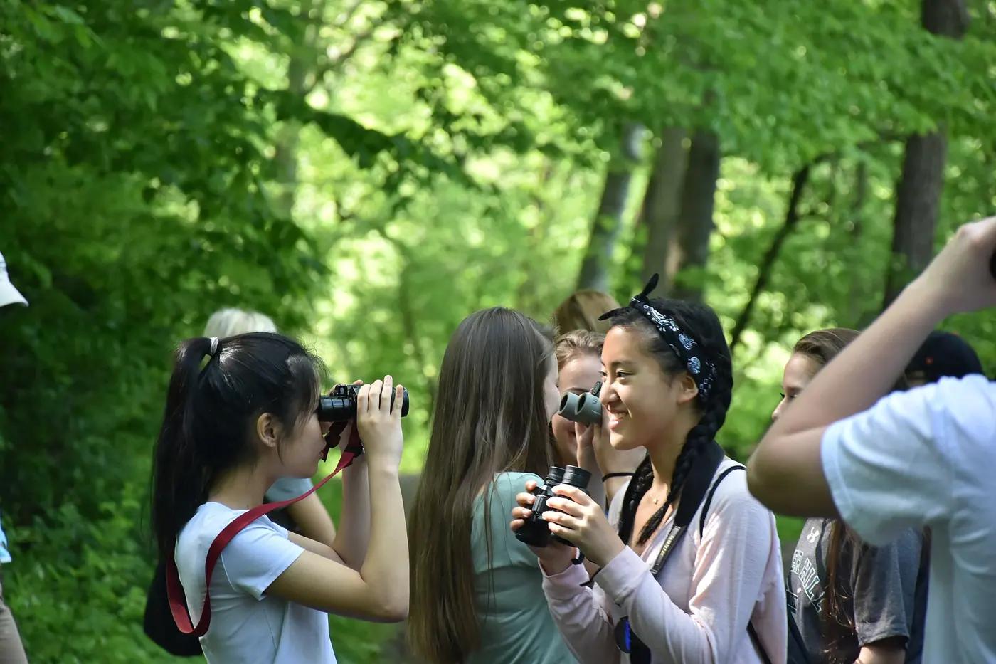 Young birdwatchers looking through binoculars in a green woodland
