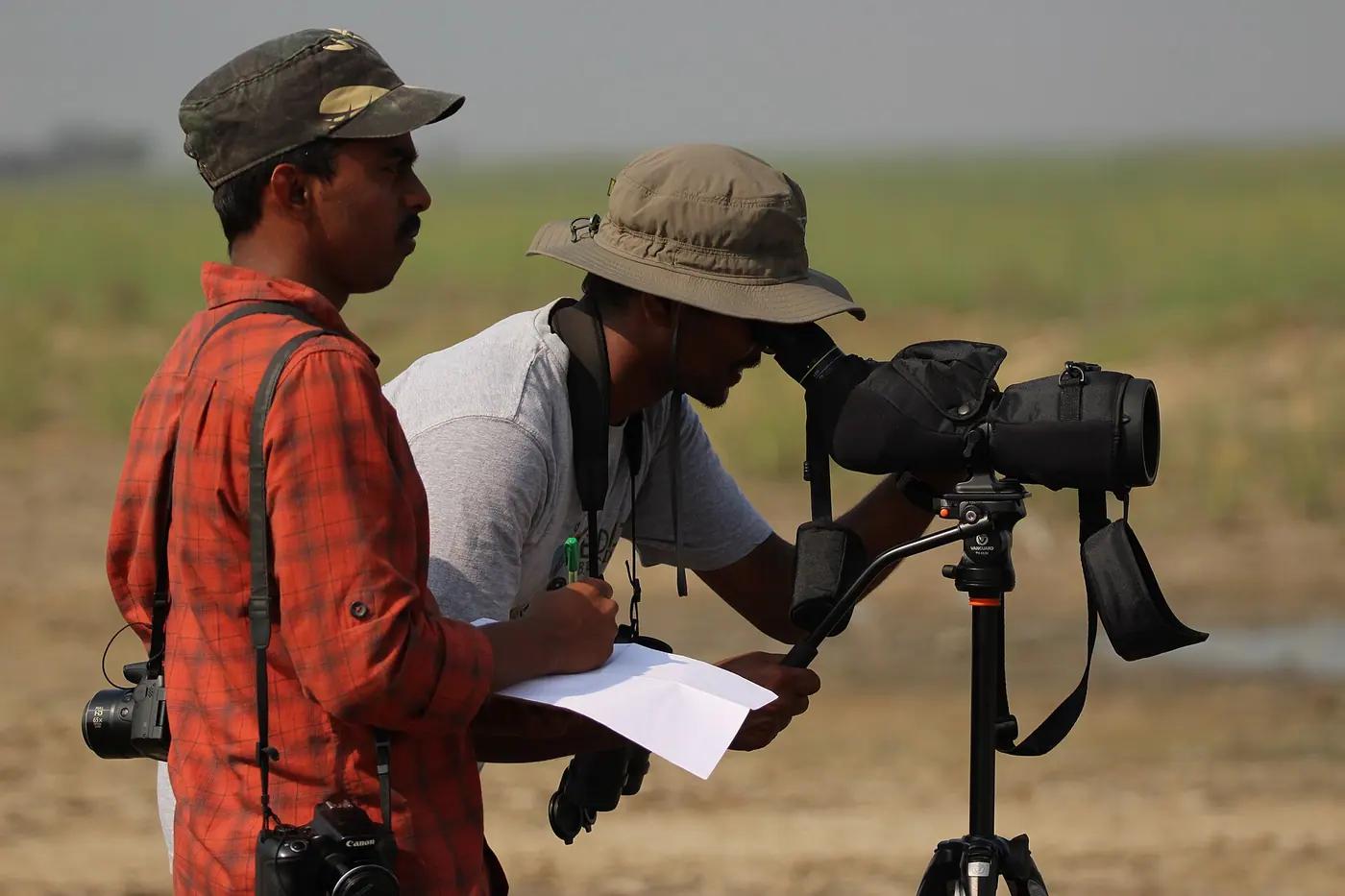 Two birdwatchers with a spotting scope recording a count on paper